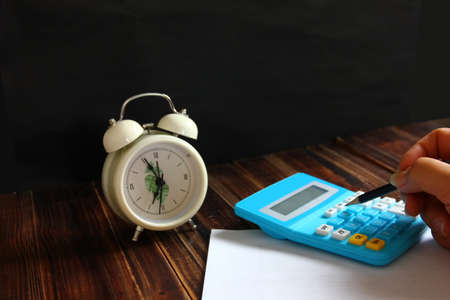hand using calculator on white paper with alarm clockの写真素材