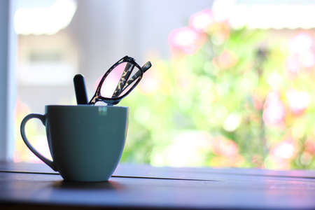 spectacles with pen in ceramic coffee cup on retro wood floor with blur backgroundの写真素材