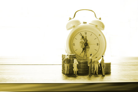 the figure people model standing in front coins stack with alarm clock background, people saving money conceptの写真素材