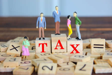 the figure people modle standing on wood block. text TAX on wood cube on numbersの写真素材