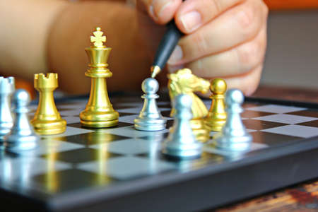 golden king chess among chess pieces on board with blur hand holding black pen