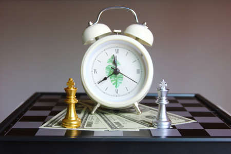 king golden and silver chess on American bank note on chess board with white alarm clock , business conceptの写真素材