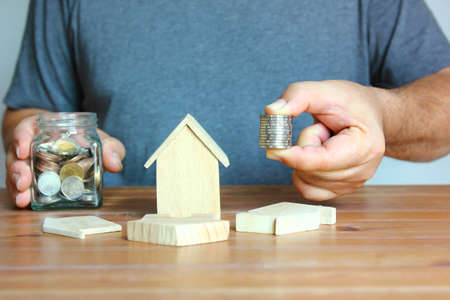 man saving coins with wood model home on wood floor , business home concept