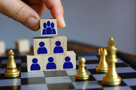 hand holding wood block with group of blue people icon put on the top of wood block stack, team work conceptの写真素材