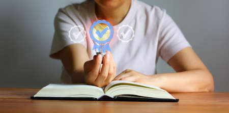 Asian woman holding light bulb over book on table with illustration guarantee icon , education...