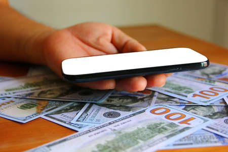 hand holding mobile phone in hand on American dollar bank note with copy spaceの写真素材