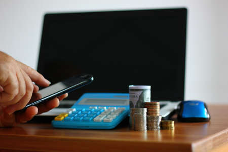 coins stack on wood table  while worker us ing mobile phone searching money information , money...