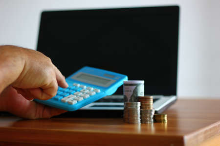 coins stack beside laptop with worker us calculator , money conceptの写真素材