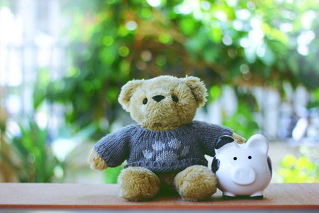 brown teddy bear put on  gray sweatertouching black and white piggy bank green abstract background