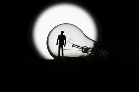 silhouette business man standing in front of light bulb moon white glowing isolate on blackの写真素材