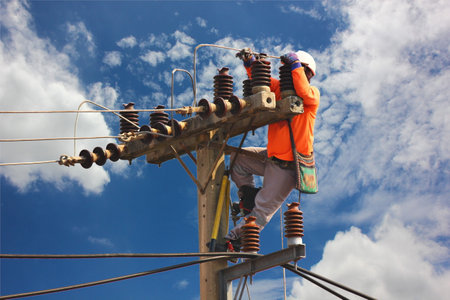 electric worker repair high voltage transmission lines on pole against blue skyの写真素材