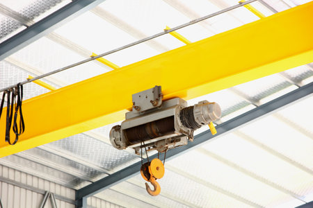 electric overhead crane install on yellow metal beam in warehouse. dictribution centers use cranes to move large quantities of heavy goods at onceの写真素材