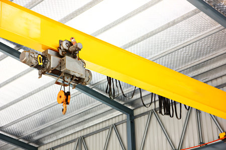 electric overhead crane install on yellow metal beam in warehouse. dictribution centers use cranes to move large quantities of heavy goods at onceの写真素材