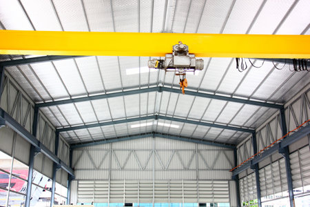 electric overhead crane install on yellow metal beam in warehouse. dictribution centers use cranes to move large quantities of heavy goods at onceの写真素材
