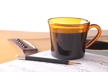 cup of black coffee with music notes and pencil on acoustic guitarの写真素材