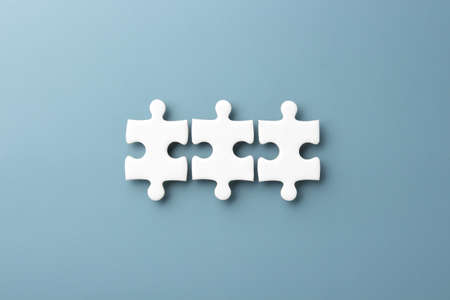 white jigsaw puzzle pieces on blue paper background with copy space