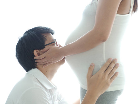 Happy young asian man kissing the belly of his lovely pregnant wife isolated on white background.の写真素材