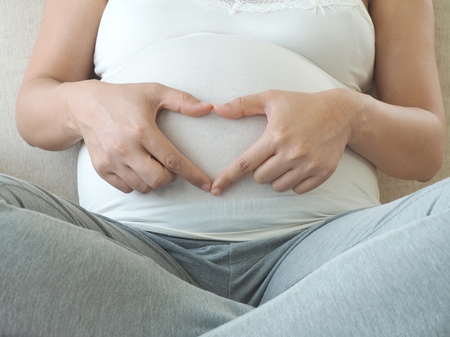 Pregnant woman holding her fingers in heart shape. Maternity concept and Baby Shower.の写真素材