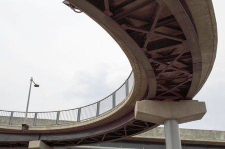 looking up from under a curved steel and concrete walkway crossingの写真素材