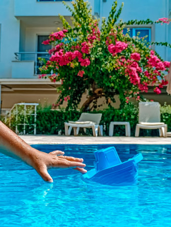The hand of child holding blue boat in the pool on background of pink flowers