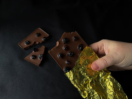 Dark chocolate broken with blueberries on a black background. View from above.