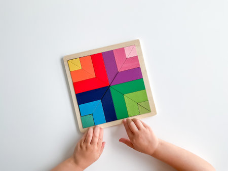 childs hand collects multicolored wooden mosaic on white background.