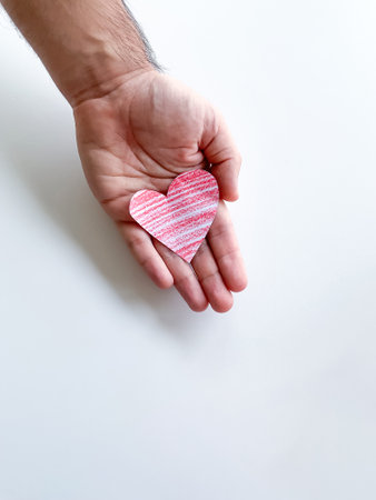 A mans hand holds a red paper heart on a white background. Empty space for an