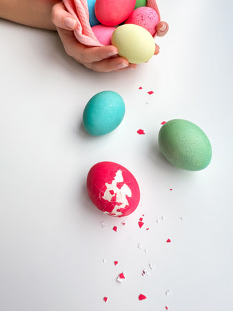 Hands holding colorful painted Easter eggs with one cracked egg on the side, representing Easter...
