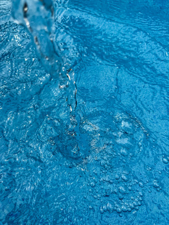Background dynamic splash of clear water creating swirling wave in blue water with droplets...