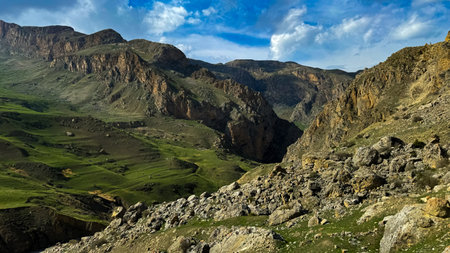 Mountain landscape with green valleys, rugged cliffs under blue sky with clouds. For advertising...