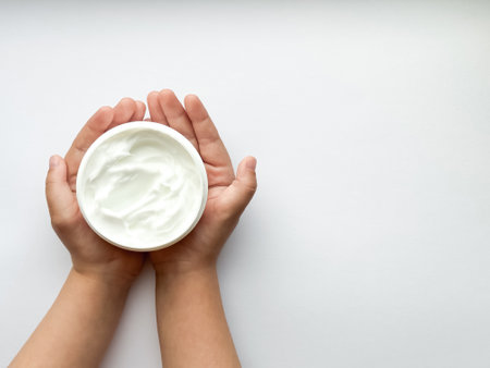 Close up of childs hands holding container of hand cream on white background with copy space. Skincare and moisturizing concept. Design for healthcare and wellness.の写真素材