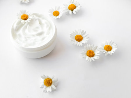 Open jar of white hand or body cream with chamomile flowers on white background. Flat lay composition. For skincare and beauty product concept.の写真素材