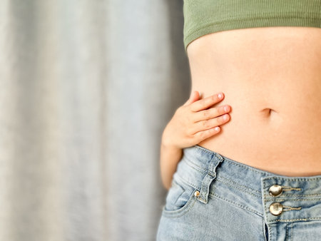 Close up of woman in jeans and green top with childs hands around her waist. Concept of family...