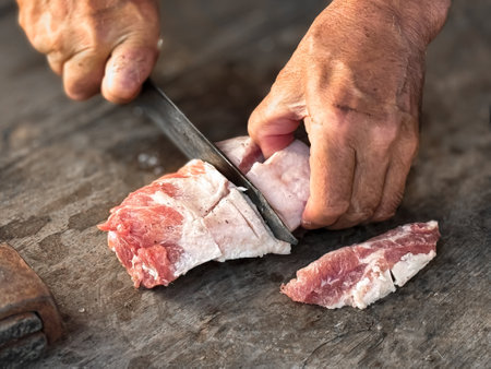 Hands skillfully cutting raw meat on wooden surface for culinary preparationの写真素材