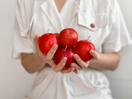 Woman holding fresh red apples in hands against white blouseの写真素材