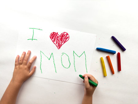 Childs hand draws heartfelt I love mom with colorful crayons on white paperの写真素材