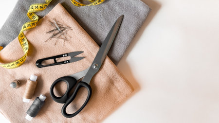 Sewing tools and fabrics. Scissors, thread, measuring tape, needles, and pins on soft clothの写真素材