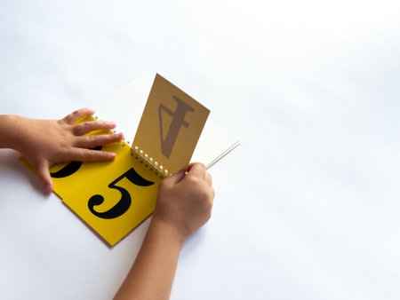 A child turns a page of learning numbers to the next number on a bright yellow backgroundの写真素材