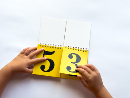 Child flipping yellow calendar pages with numbers on white backgroundの写真素材