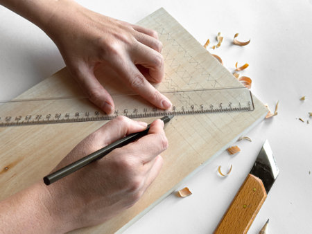 Hands drawing geometric patterns on wood with pencil and ruler