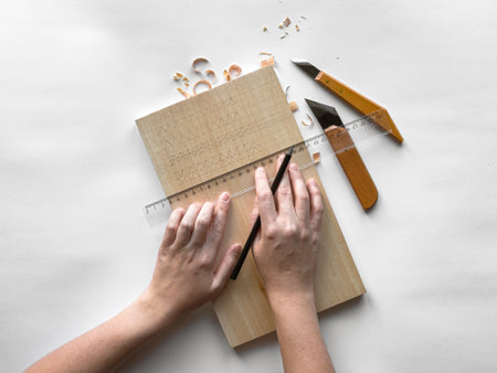 Precision wood carving: hands sketching patterns on wood with knives and rulerの写真素材