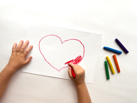 Child drawing heart with crayons on white paper. Creativity and expressionの写真素材