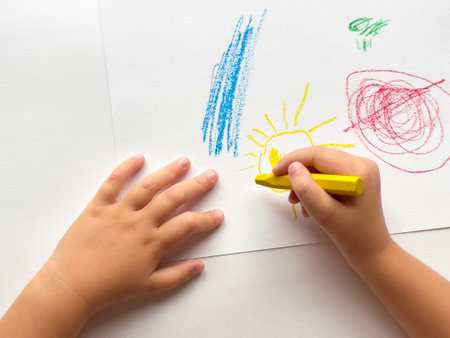 Childs hand drawing colorful crayon sun on white paper