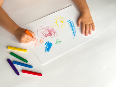 Child drawing with colorful crayons on white paper