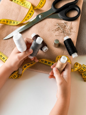 Hands holding thread and sewing tools on fabric with measuring tape and scissors