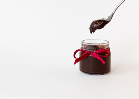 Chocolate spread in jar with red ribbon and spoon on white backgroundの写真素材