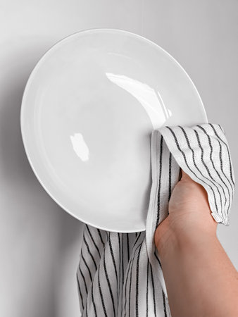 Hand drying white ceramic plate with striped cloth in kitchen setting