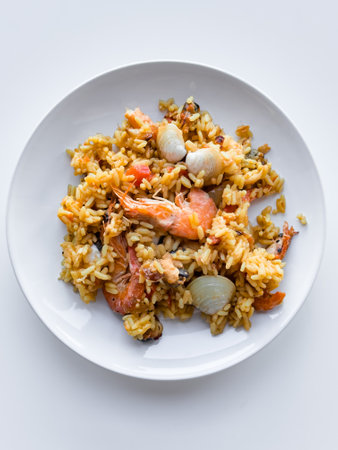 Delicious seafood paella with shrimp, mussels, and rice on a white plateの写真素材