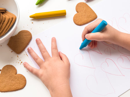 Child drawing hearts with crayons near heart shaped cookies on a tableの写真素材