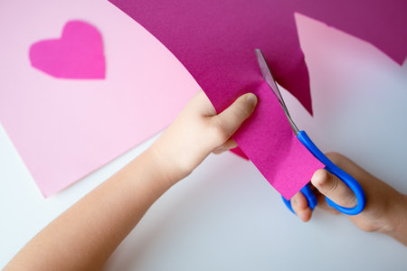 Child crafting. Hands cutting pink paper with scissors for heart art projectの写真素材